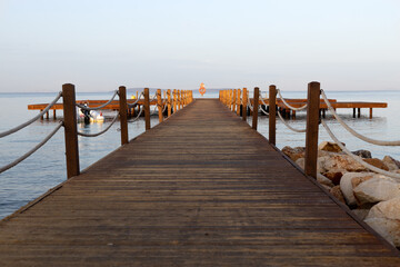 Wooden pier going into the blue sea at dawn.