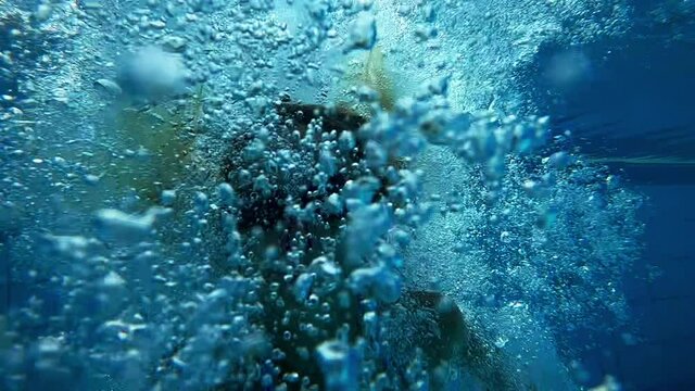 A woman in swimming goggles and with a clip on her nose jumps into the pool underwater. Slow motion hd video.