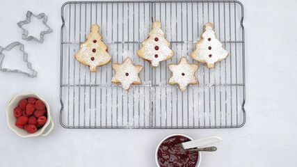 Homemade Christmas cookies with raspberry jam and powdered sugar topping close up on cooling rack directly from above