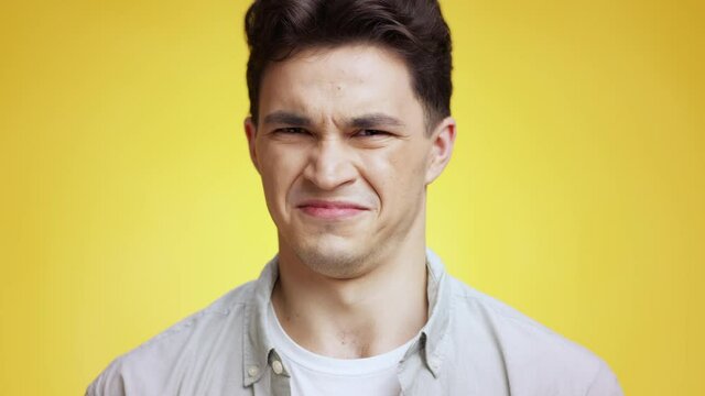 Awful smell. Young man feeling disgusting odor and squinting his nose, shivering in aversion, yellow studio background