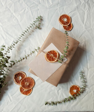 Overhead view of a package wrapped in brown paper with a blank envelope and rustic eucalyptus and orange decorations