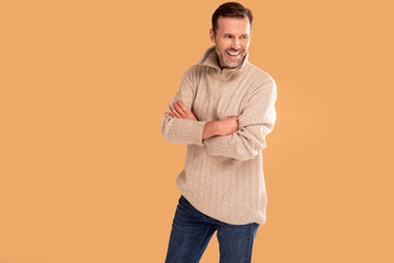 Handsome man with beard wearing casual sweater and jeans standing over studio background smiling.