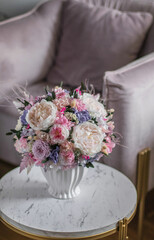 Beautiful preserved flower bouquet in ceramic vase on white table near light pink armchair.