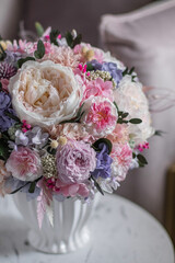Beautiful preserved flower bouquet in ceramic vase on white table near light pink armchair.