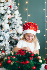 Santa little helper with decorative christmas tree on background. Little smiling girl make...