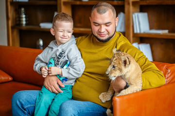 Obraz premium Father and son play with little lion cub in the room