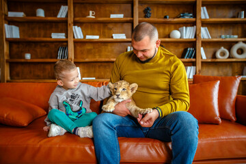Obraz premium Father and son play with little lion cub in the room
