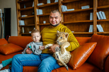 Obraz premium Father and son play with little lion cub in the room