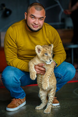 Man playing with a young lion cub in the room
