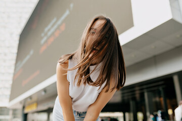 Carefree happy young lady with dark hair covering face by hair posing at camera and feel freedom outside