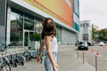 Romantic brunette woman jumping with shy smile outdoor. Portrait of blithesome caucasian girl having fun outside