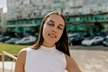 Outdoor portrait of charming pretty woman with bright holiday make up walking on the sunny street in big city