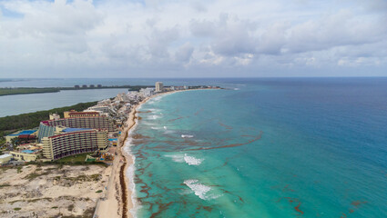 Aerial view. Resort town, sandy beaches, tall houses, hotels. The turquoise water near the shore is polluted with algae. Cloudy sky. Climate change, global warming. Poisoning with wildlife toxins.