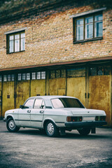 Fototapeta na wymiar Photo of old car standing before rusty gate of building