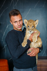 Young man holding a little lion cub in his arms