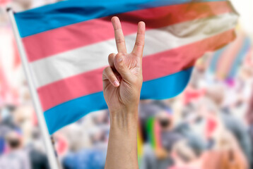 Supporting hand makes the peace sign with a transgender flag in a parade - obrazy, fototapety, plakaty