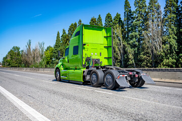 Bright green powerful big rig semi truck tractor without the semi trailer running on the wide...