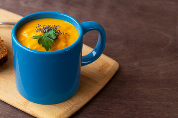 Pumpkin cream soup in a blue mug with bread on the dark wooden background. vegetarian soup-puree with cream, croutons on the cutting board with copy space