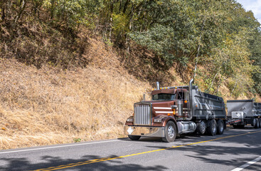 Brown big rig tip semi truck with two tipper trailers driving on the narrow road at Columbia Gorge...