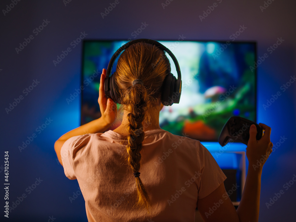 Wall mural blonde girl gamer is playing a video game. she has headphones on her head, a joystick in her hand. l