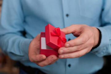 A half-open red box with a bow in the hands of a man in a blue shirt