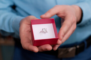 A red box with a white gold ring and a precious stone in the hands of a man in a blue shirt