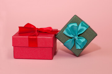 A red box with a red ribbon and a green box with a blue bow on a pink background