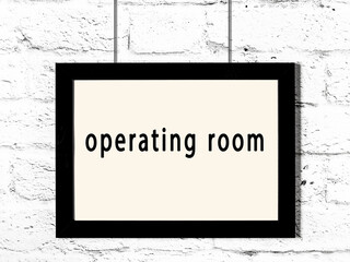 Black frame hanging on white brick wall with inscription operating room