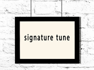 Black frame hanging on white brick wall with inscription signature tune
