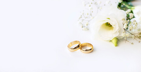 White flowers and two golden wedding rings on white background.
