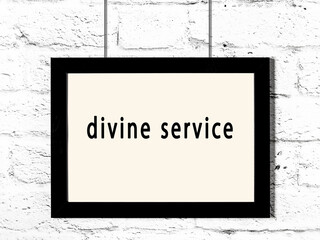 Black frame hanging on white brick wall with inscription divine service