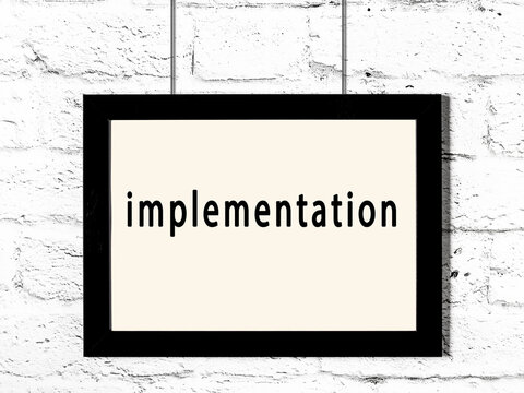 Black frame hanging on white brick wall with inscription implementation
