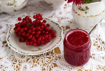 Healthy jam from viburnum berries (Viburnum opulus) in a glass jar, a bunch of viburnum, antique dishes and chrysanthemums in a vase. Preparations for the winter from colds