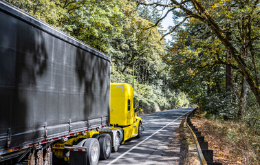 Classic powerful yellow big rig semi truck tractor transporting cargo in industrial covered black...