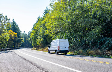Compact cargo commercial mini van driving on the turning road with forest on the sides