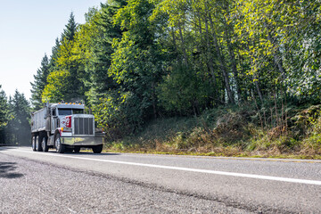 Fototapeta na wymiar Compact powerful big rig tipper semi truck running on the road to working side