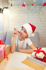 The child writes a letter to Santa Claus. There are Christmas gifts nearby. Bright interior. New Year's Eve. Vertical orientation.