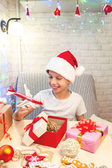 A laughing child in a Santa Claus hat received a plane as a Christmas gift. Christmas interior of the house.