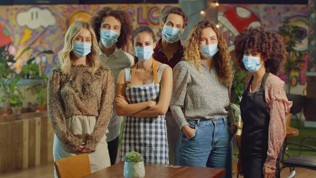 Portrait of multi-cultural team of servers bar staff and owner wearing face masks during health pandemic standing in cool bar or club - shot in slow motion