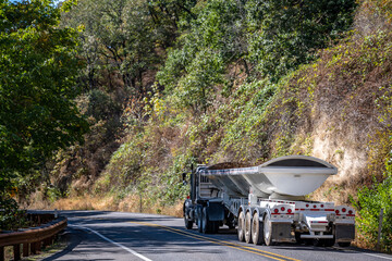 Day cab big rig tip semi truck with long tipper semi trailer running on the winding mountain road...