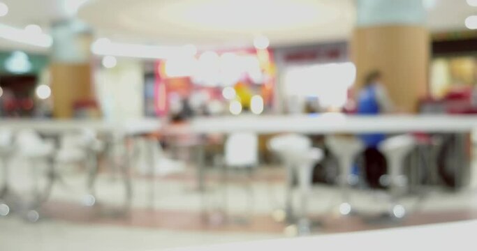 People eat in a large shopping mall food court sitting at tables as defocused background timelapse.
