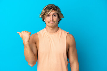 Handsome blonde man isolated on blue background unhappy and pointing to the side