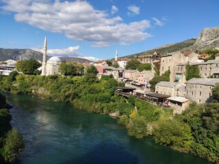 Fototapeta na wymiar La village de Mostar en Bosnie-Herzégovine, avec ses maisons ou habitations colorés, sa végétation verte, sur les bords du fleuve Neretva, ancienne province Ottoman