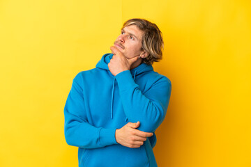 Handsome blonde man isolated on yellow background having doubts