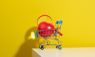 red heart in a miniature metal trolley from the store on a yellow background. Organ donation, transplant concept