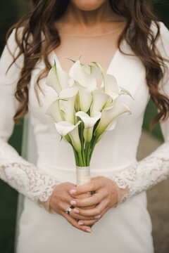 The bride is holding a bouquet in her hands. Elegant white wedding bouquet. Bride holding a bouqet of calla lilies.