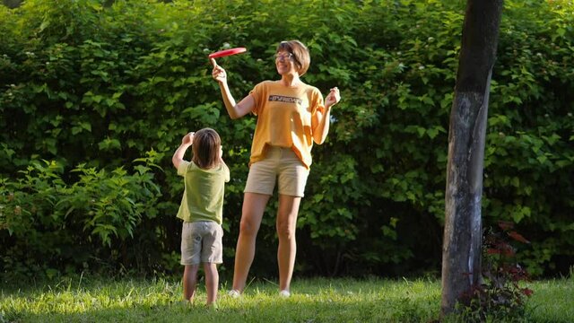 Mother and son play frisbee on grass lawn. Summer vibes. Outdoor leisure activity. Family life. Sports game at backyard.