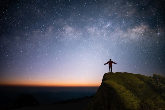 Silhouette of young traveler and backpacker watched the star, milky way and beautiful view night sky alone on top of the mountain. He enjoyed traveling and was successful when he reached the summit.