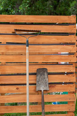 A rusty shovel and a rake leaning on a old wooden fence