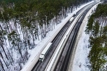 white trucks on the higthway. convoy  whith cargo driving by road seen from the air. Top view landscape. shooting from a drone. Cargo delivery in winter. Aerial view of snowy road in winter forest